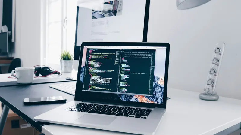 Laptop showing code on a desk beside a monitor
